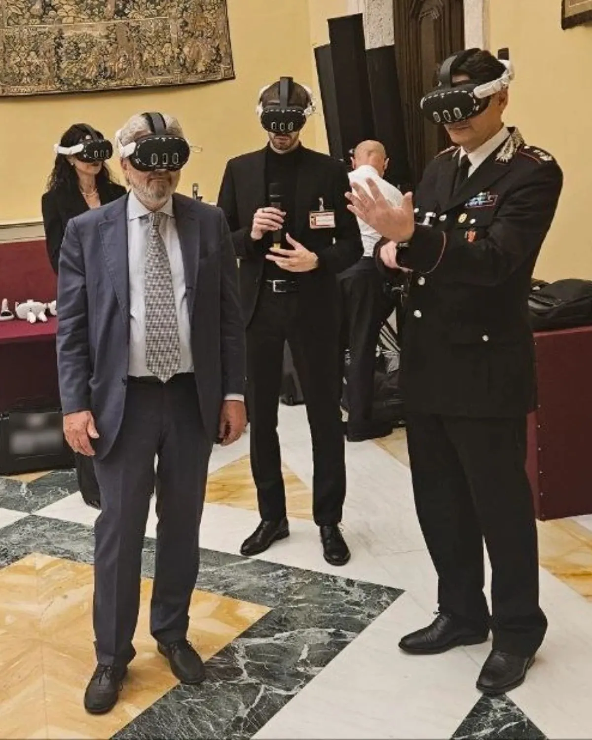 Ospiti, tra cui un ufficiale in uniforme, provano con il visore una simulazione di formazione in una sala istituzionale